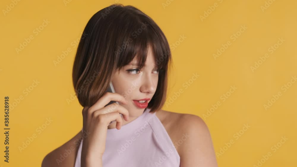 Attractive brunette girl with bob hair talking with best friend on phone discussing news isolated on yellow background. Always in touch Attractive brunette girl with bob hair talking with best friend on phone discussing news isolated on yellow background. Always in touch