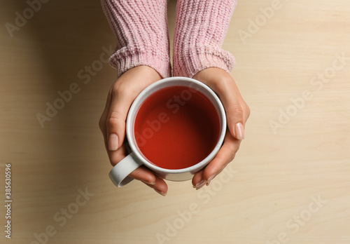 Woman holding cup of tea at wooden table, top view