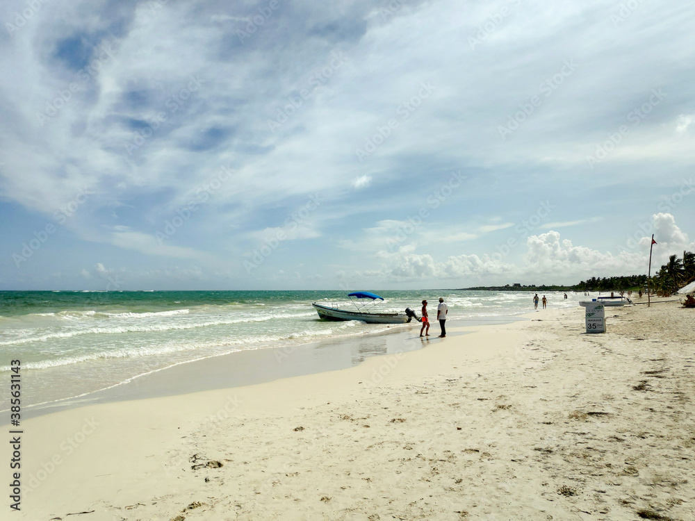 La playa de Tulum, en el caribe mexicano, una barca y dos personas con un cielo nublado como fondo.
