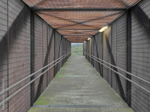 Interior de un puente peatonal con estructura met  lica a base de armaduras de acero  base de concreto y malla perimetral. Vista horizontal
