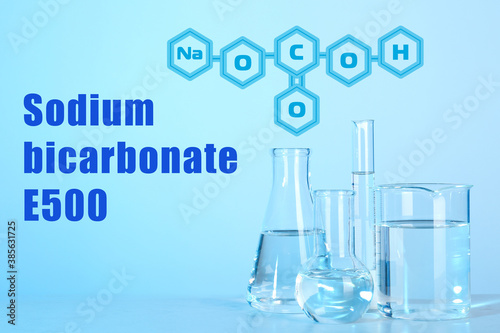 Text Sodium bicarbonate E500 with soda formula and laboratory glassware on background
