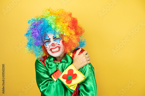 Clown standing over yellow insolated yellow background with pain on her shoulder and a painful expression