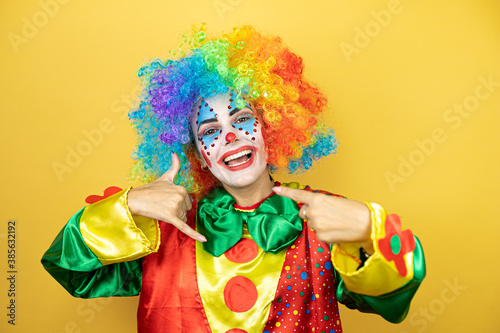 Clown standing over yellow insolated yellow background doing the “call me” gesture with her hands.