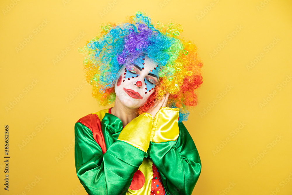 Clown standing over yellow insolated yellow background sleeping tired dreaming and posing with hands together while smiling with closed eyes. Clown standing over yellow insolated yellow background sleeping tired dreaming and posing with hands together while smiling with closed eyes.