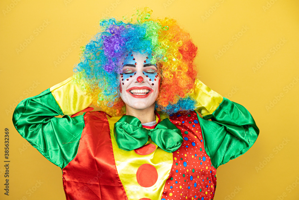 Clown standing over yellow insolated yellow background relaxing and stretching, arms and hands behind head and neck smiling happy Clown standing over yellow insolated yellow background relaxing and stretching, arms and hands behind head and neck smiling happy