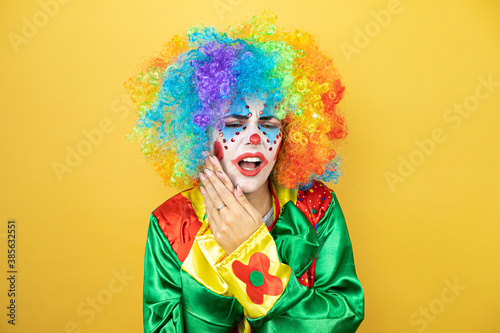 Clown standing over yellow insolated yellow background touching mouth with hand with painful expression because of toothache or dental illness on teeth