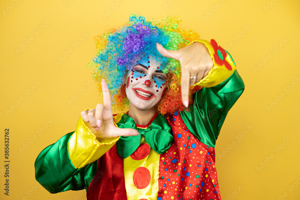 Clown standing over yellow insolated yellow background smiling making frame with hands and fingers with happy face