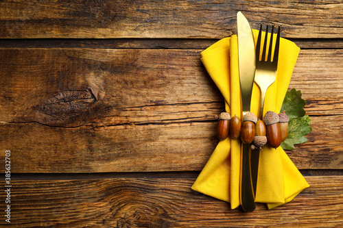Seasonal table setting with autumn decorations on wooden background. Cutlery with acorns and space for text, top view