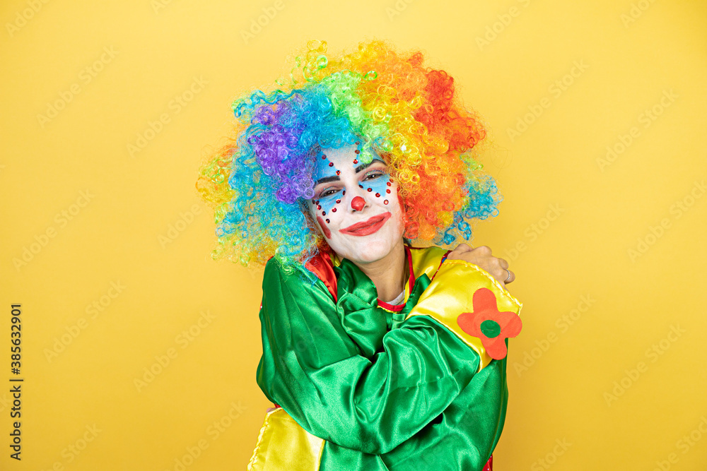 Clown standing over yellow insolated yellow background hugging oneself happy and positive, smiling confident Clown standing over yellow insolated yellow background hugging oneself happy and positive, smiling confident