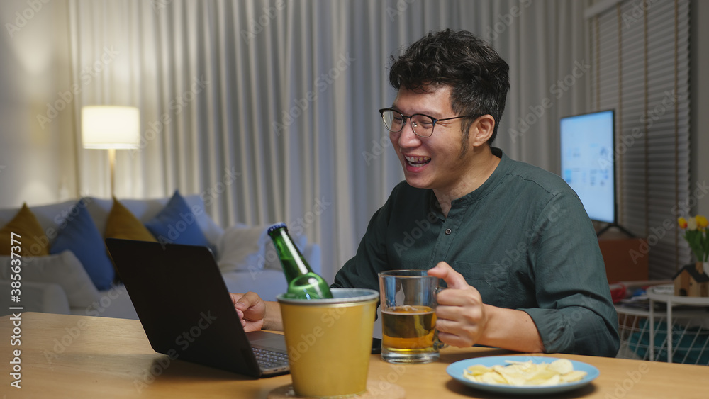 Attractive young happy asian man enjoy relax night party event online celebration festive with friends at house clinking beer with glass and bottle toasting drinking via video call. Attractive young happy asian man enjoy relax night party event online celebration festive with friends at house clinking beer with glass and bottle toasting drinking via video call.