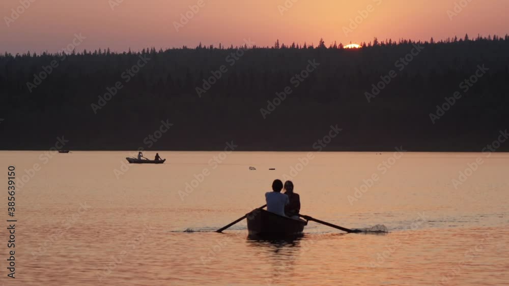 A couple sailing on the boat using paddles on sunset A couple sailing on the boat using paddles on sunset