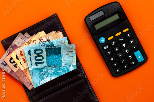 Brazilian money in wallet, with notepad, pen and calculator. Finance and salary concept. Economy of Brazil. Orange background