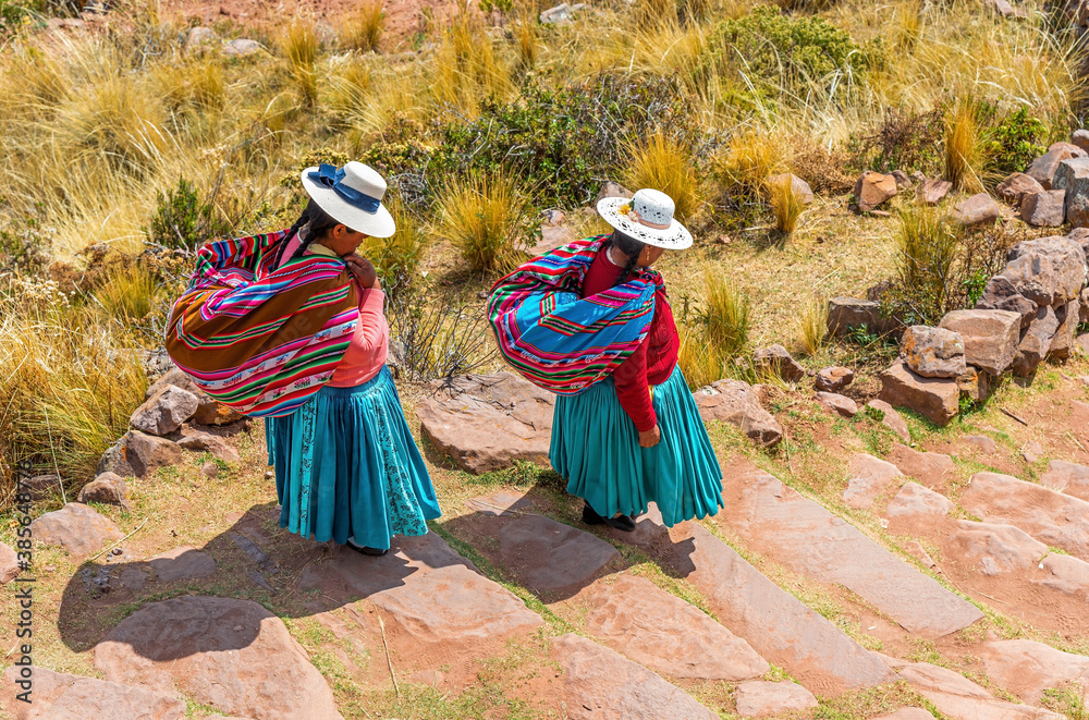 Fototapeta Two Quechua indigenous women in traditional clothing and textile walking down steps, Taquile island, Titicaca Lake, Puno, Peru.