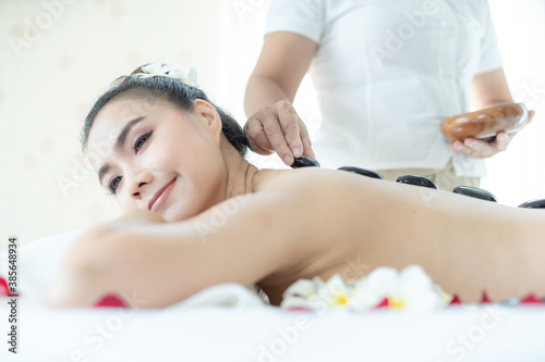 A spa masseuse is placing a hot stone on an Asian woman. Lying in a relaxing massage spa.