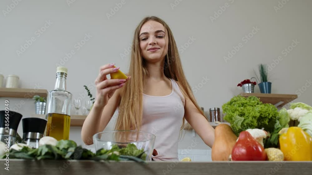 Vegan girl cooking salad with raw vegetables, adding lemon juice. Squeeze a lemon fruit in hands Vegan girl cooking salad with raw vegetables, adding lemon juice. Squeeze a lemon fruit in hands