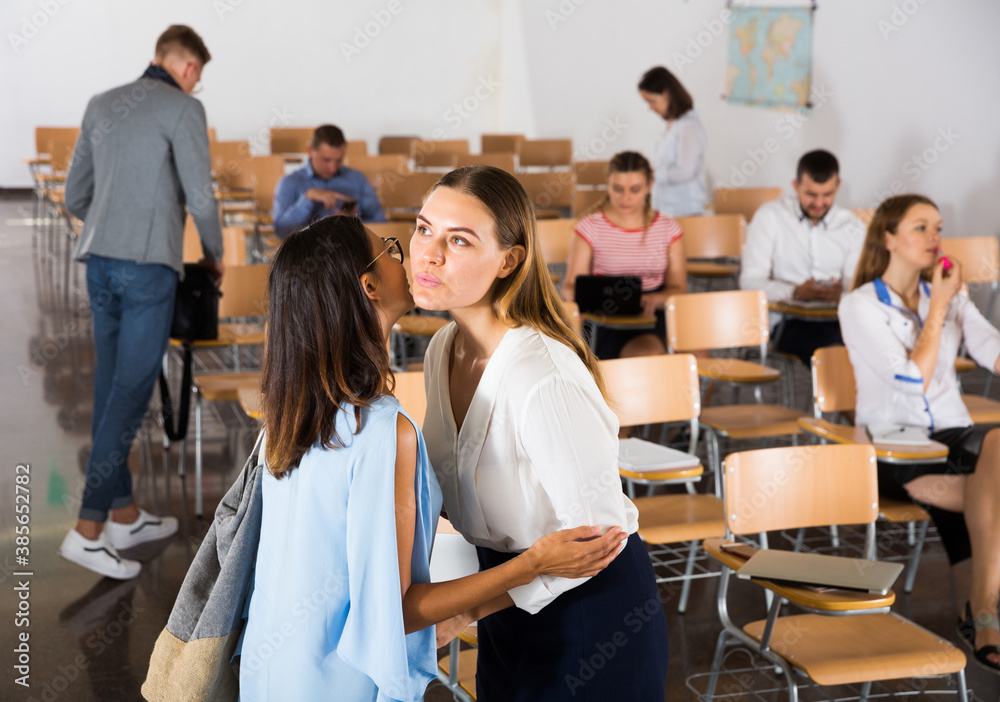 Obraz premium Portrait of two young women meeting in lecture hall, kissing each other on cheek..