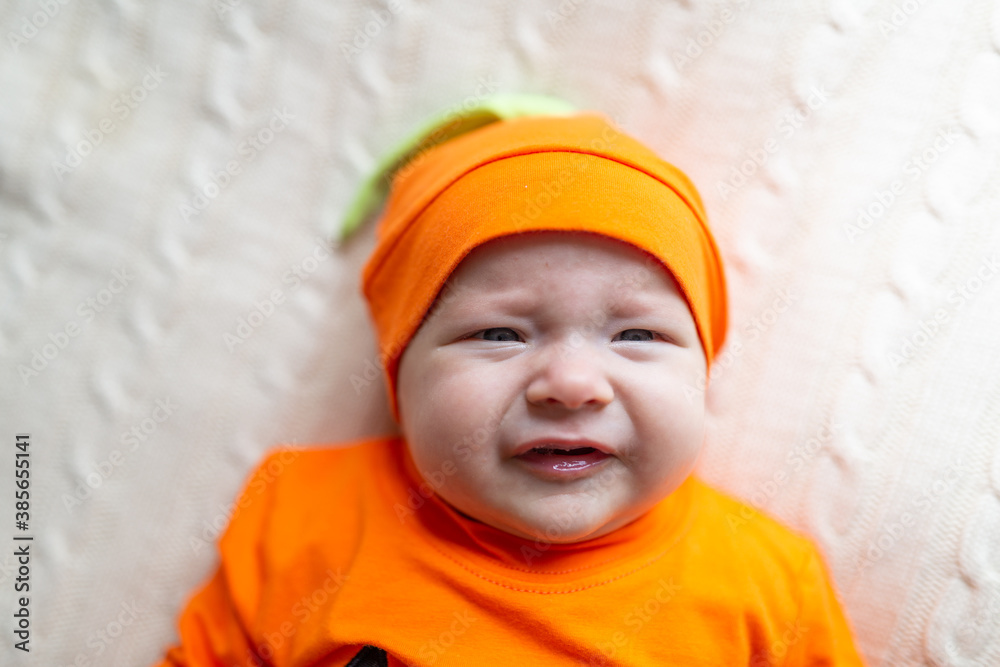 High Angle View Of Baby In Pumpkin Costume. Happy Kid two months old in orange Halloween costume on bed High Angle View Of Baby In Pumpkin Costume. Happy Kid two months old in orange Halloween costume on bed
