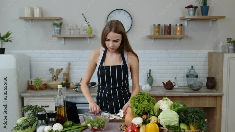 Vegan girl cooking salad with raw vegetables while looking on digital tablet for online recipe Vegan girl cooking salad with raw vegetables while looking on digital tablet for online recipe