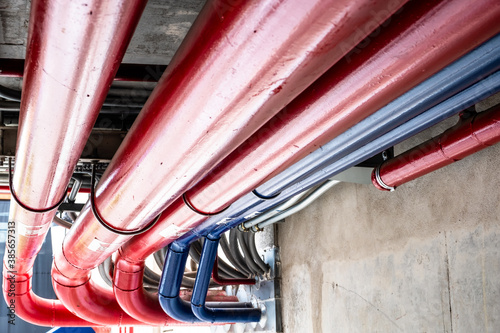 Red and blue metal water pipes installed to white concrete ceiling of a building.
