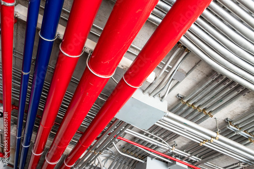 Rows of metal conduit pipes installed to the ceiling of a building. Red and blue water pipes for fire extinguishers and drainpipes.
