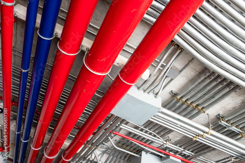 Rows of metal conduit pipes installed to the ceiling of a building. Red and blue water pipes for fire extinguishers and drainpipes. 
