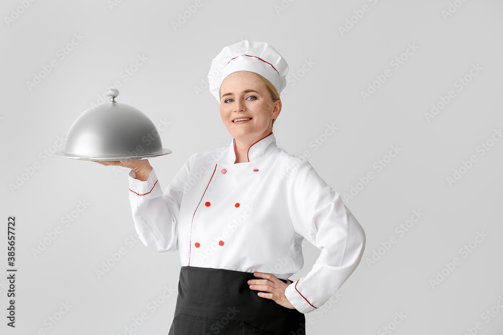 Mature female chef with tray and cloche on grey background Mature female chef with tray and cloche on grey background