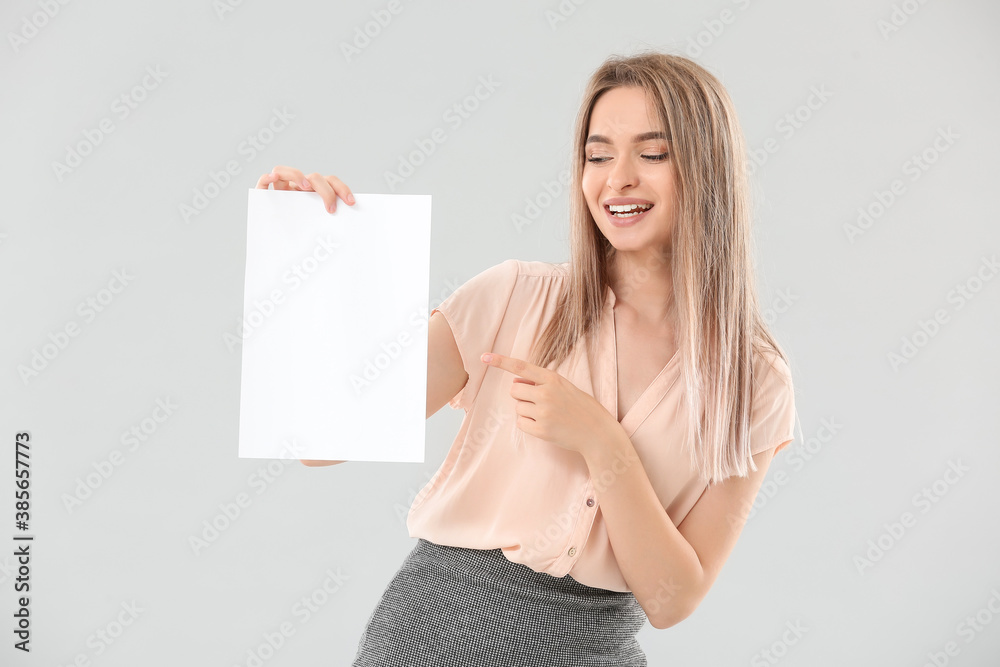 Naklejka premium Young woman with blank paper sheet on light background