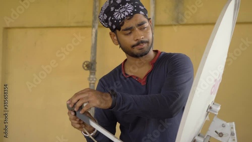 indian boy with hair band bandana fixing dish antina tv airtell checking signal photo