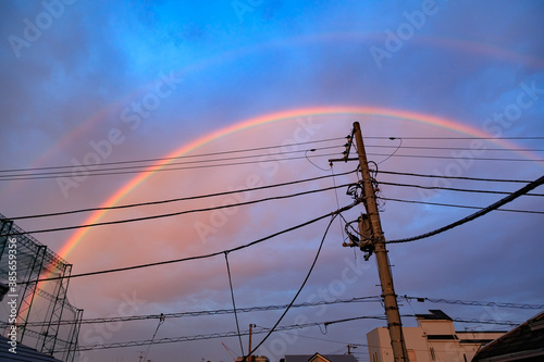 住宅街の雨上がりの朝焼けの虹と電線