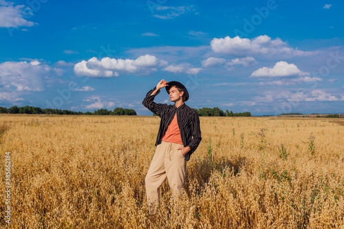 Tall handsome man with black hat standing at golden oat field. © Smile