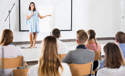 Smiling female coach giving presentation for adult audience in lecture hall .. © JackF