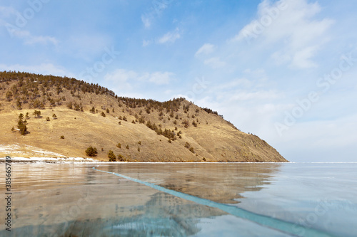 Baikal Lake on a cold winter day. View from the ice to the beach and coastal hills in Kharyuzovaya Bay. Ice travel and hiking (focus on the shore, ice out of focus). Natural winter background