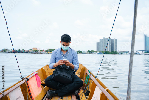 Business man wear mask travel by a boat in Bangkok. © THESHOTS.CO