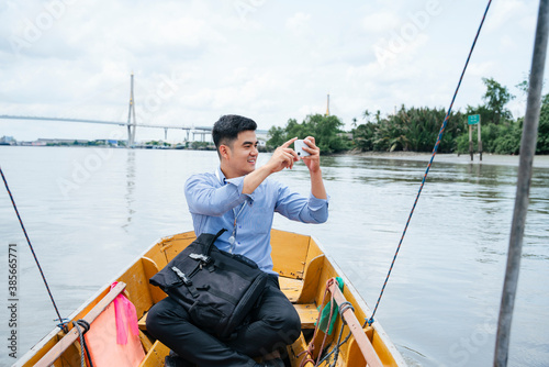 Business man taking photo with smartphone and travel by a boat in Bangkok. © THESHOTS.CO