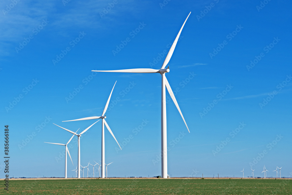 A row of windmills has been installed in a green field and is silhouetted against a blue sky. A row of windmills has been installed in a green field and is silhouetted against a blue sky.