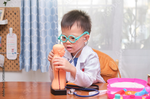 Asian school boy in doctor uniform playing doctor at home, kid wearing stethoscope learning and play with anatomical body organs model, Role playing Ideas for kids concept