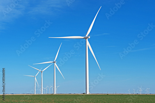 A row of windmills has been installed in a green field and is silhouetted against a blue sky.