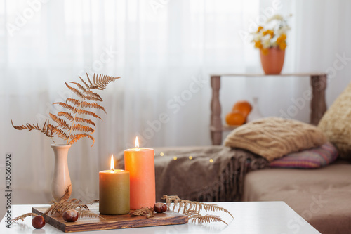 burning candles with autumn decor on white table at home