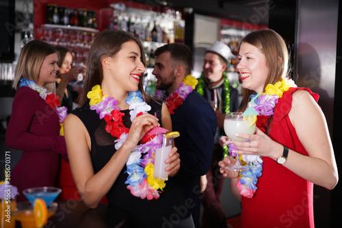 Happy young female colleagues enjoying company party in Hawaiian style in bar