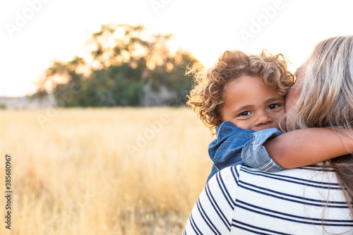 The face of an adorable curly haired African American boy in the arms of his mother in the outdoor sunlight. A happy and content expression as the mom shows love and affection to her son