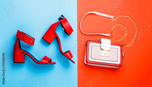 Stylish red women's leather sandals shoes. Woman bag, sandals on red and blue background isolation. Ladies bag and stylish red shoes. High heel women shoes and a bags