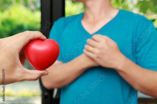 Red heart ball foam on hand with man clutching his chest from acute pain. Heart attack symptom-Healthcare and medical concept.