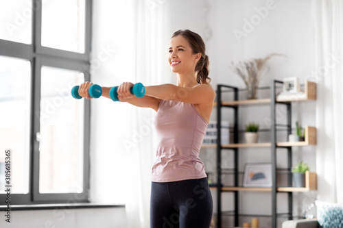 fitness, sport and healthy lifestyle concept - smiling young woman with dumbbells exercising at home