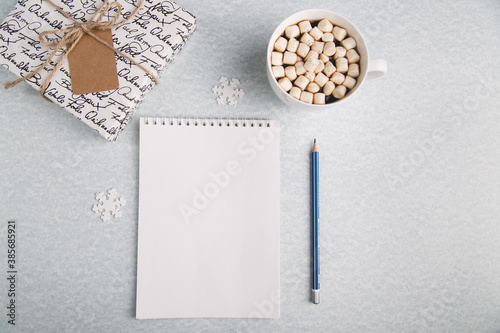 A clean notebook lies on a light background, next to a pencil, a mug with coffee and a gift. For recording ideas, planning, summing up the results of the year. Horizontal photo.