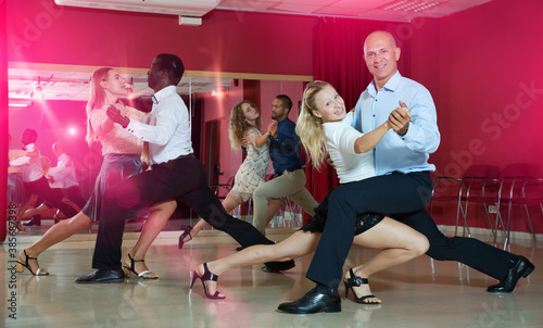 Smiling adult pairs dancing tango movements in modern dance studio