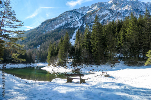 Benches at the shore of Green Lake, Austrian Alps. The lake shimmers with many shades of green and turquoise. Winter in the mountains. There is snow on the ground. Serenity