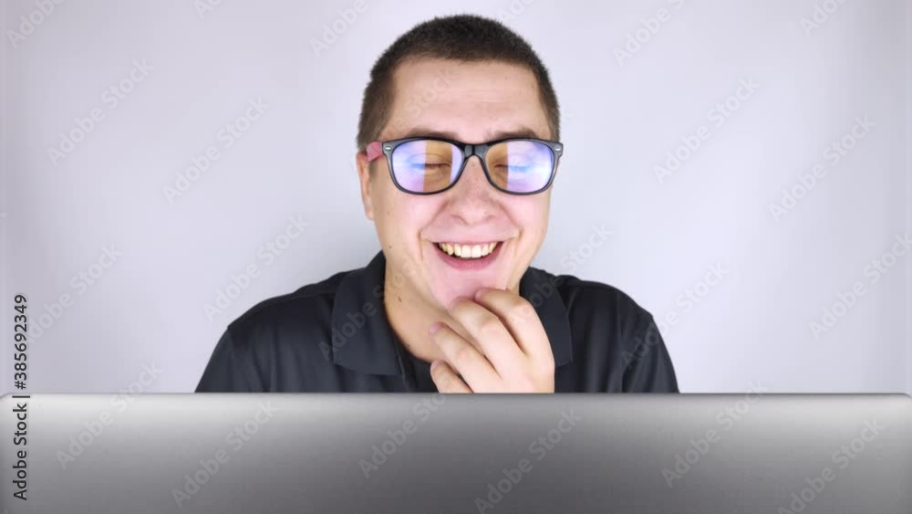 The man looks into the laptop, laughs and is surprised at what he saw there. Expression of emotions and reaction to what you see on the Internet. The concept of shocking content. The man looks into the laptop, laughs and is surprised at what he saw there. Expression of emotions and reaction to what you see on the Internet. The concept of shocking content.