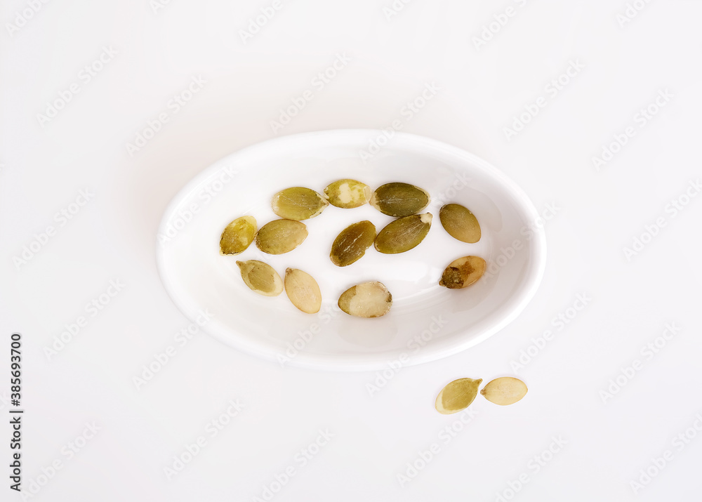 Dried pumpkin seeds in white dishes isolated on white background Dried pumpkin seeds in white dishes isolated on white background