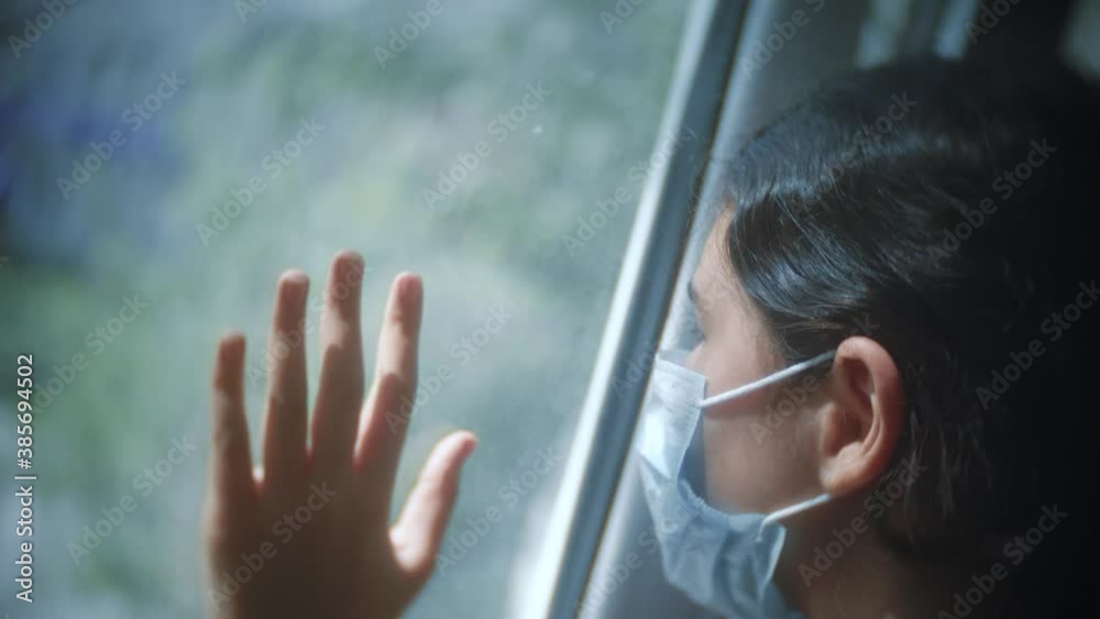 covid 19. little girl looks out the window sad in a medical gauze mask. self-isolation concept virus coronavirus pandemic infection doomsday. the girl touches lifestyle the glass sunlight wants to go covid 19. little girl looks out the window sad in a medical gauze mask. self-isolation concept virus coronavirus pandemic infection doomsday. the girl touches lifestyle the glass sunlight wants to go