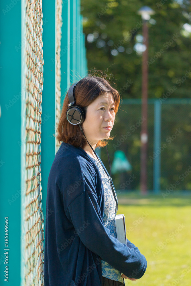 Fototapeta premium 朝の公園のグランドで本を持ってヘッドホンで音楽を聴いている女性の姿